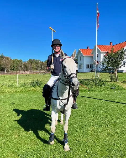 Rytter på grå hest foran det hvite gårdshuset